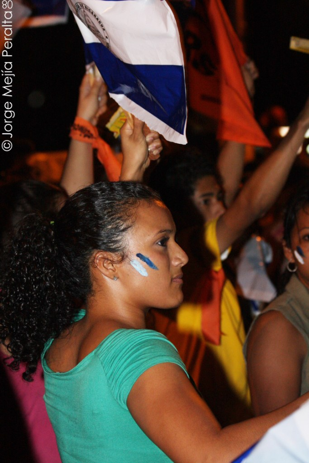 Frauen in grünen T-Shirts bei einer Demonstration, die weiße Stoffstücke halten, mit anderen Mädchen im Hintergrund.