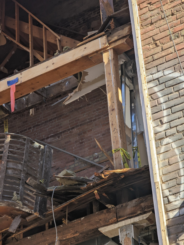 Teilweise demoliertes Gebäude mit verstreuten Holzplanken und Trömmern, zerbrochene Fenster und Türen.