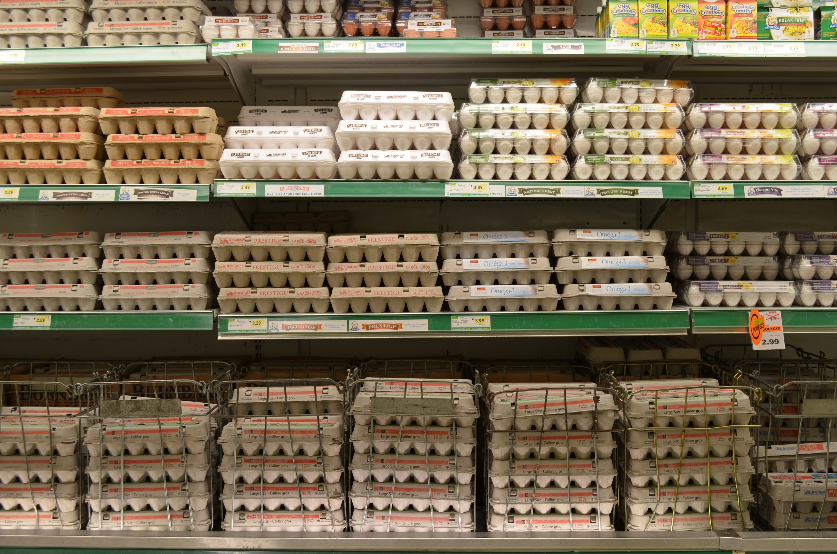 Ein Supermarktregal voller ordentlich arrangierter Eier neben verschiedenen Früchten, Gemüsen und anderen Lebensmitteln.