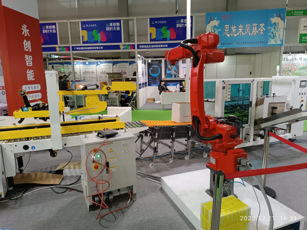 Gruppe von Robotern, die auf einem Tisch in einer Fabrikeinrichtung umgeben von Maschinen, Verdrahtung, Texttafeln und Lichtern sitzen, mit Menschen im Hintergrund.