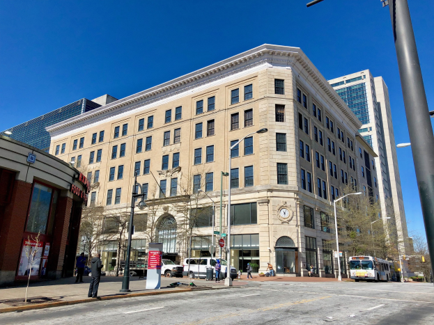 Großes Ziegelgebäude mit der Aufschrift "Washington Post Office" und vielen Fenstern, umgeben von Straßenlaternen, Lampen, Fahrzeugen, Fußgängern, Schildern, Bäumen und einem bewölkten Himmel.