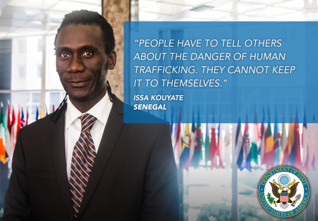 Ein Mann im Anzug und Krawatte steht vor Flaggen, mit Text auf der rechten Seite, der besagt: "Menschen müssen anderen die Gefahr der Menschenhandel mitteilen, sie können es nicht für sich behalten."