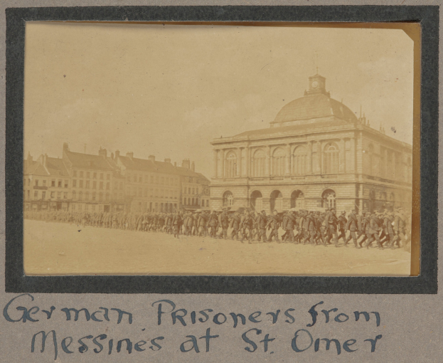 Deutsche Gefangene aus Messines vor einem Gebäude mit einem klaren blauen Himmel im Hintergrund, unten sichtbarer Text.