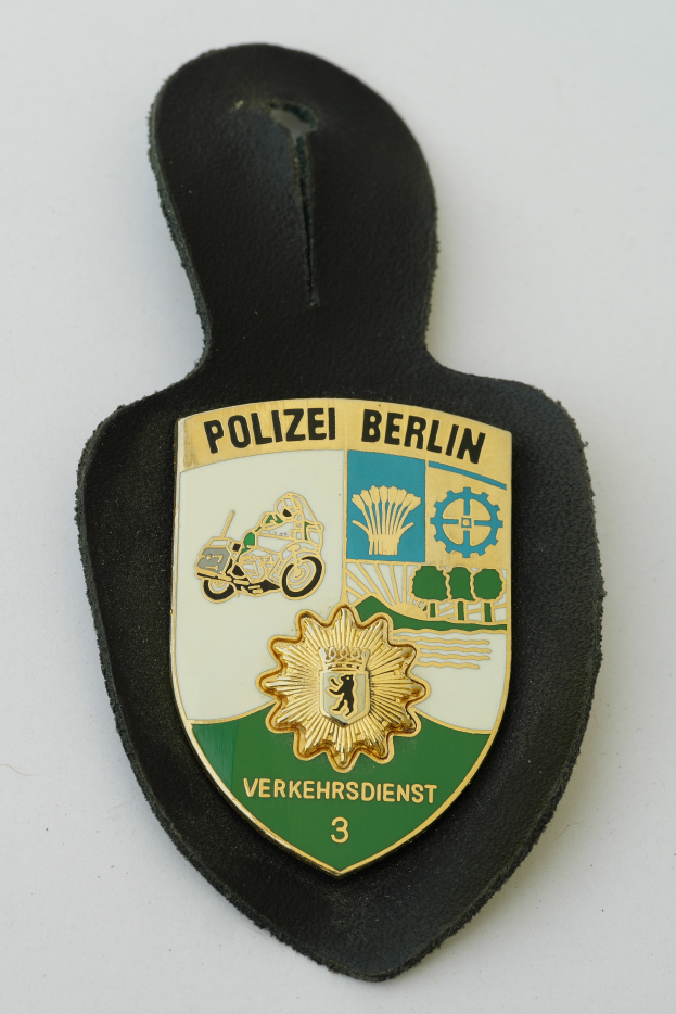 Ein Polizeistern mit der Aufschrift "Polizei Berlin" darauf, mit einem blauen Schild mit einem weißen Stern in der Mitte, umgeben von einem weißen Rand, auf einer Oberfläche plaziert.