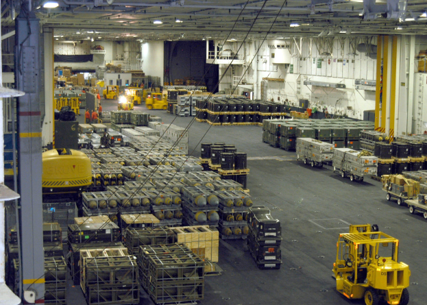 Ein großes Lager voller Numerous Trucks, Container, Menschen, Lichter, Stangen und andere Gegenstände mit einem prominenten Rad.