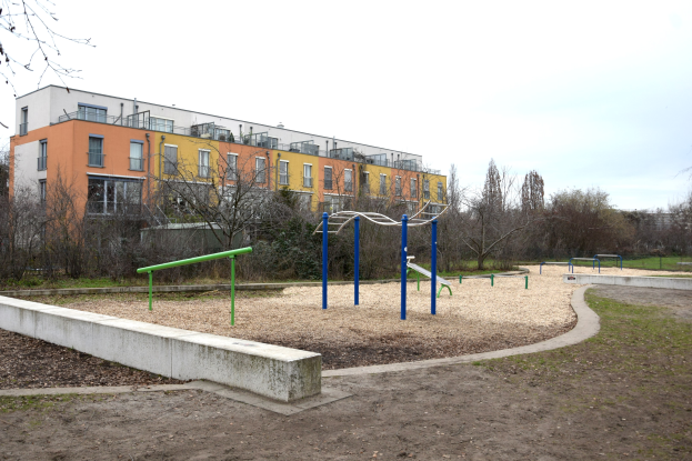 Spielplatz mit einem Gebäude, Bäumen und einem klaren blauen Himmel, auf saftig grünem Gras.