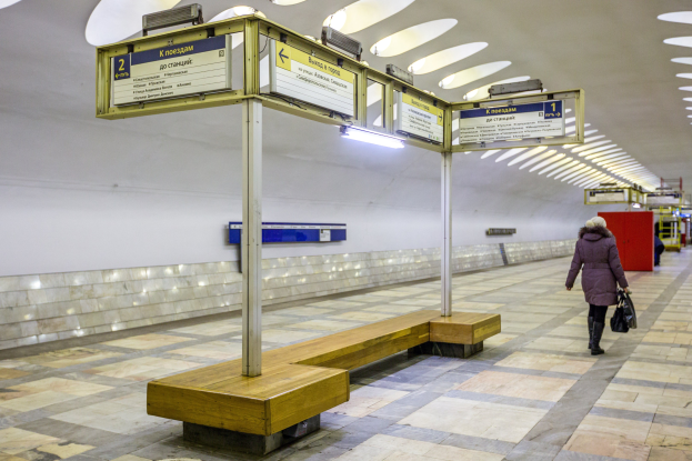 Eine Frau in einem Mantel mit einer Tasche geht durch eine Moskauer U-Bahn-Station mit Bänken, beleuchteten Tafeln und anderen Einrichtungsgegenständen.
