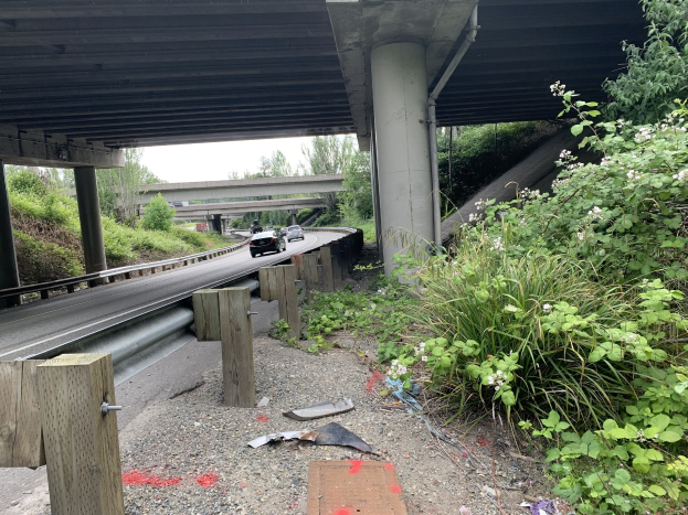Auto fährt unter einer Brücke mit Trömmern auf der Straßenseite, umgeben von Vegetation und einem klaren Himmel, wahrscheinlich nach einem tödlichen Crash auf dem I-95.