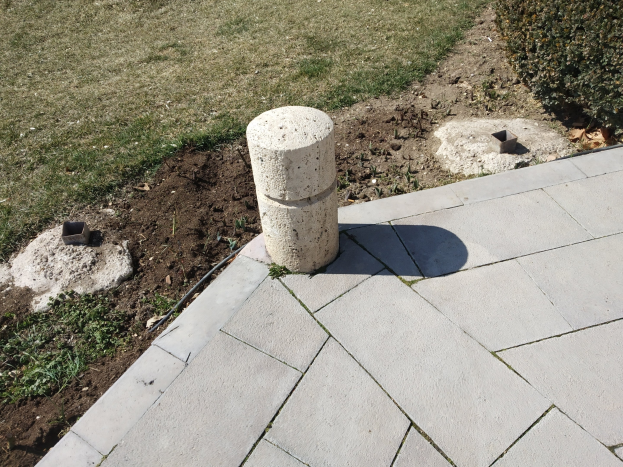 Betonsockel auf einem Ziegelweg mit umgebender grüner Gras und Pflanzen.