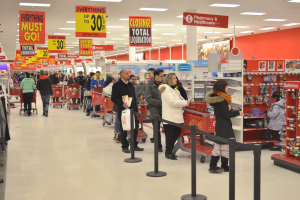 Ein volles Walmart-Geschäft mit Einkaufstüten tragenden Kunden und Einkaufswagen, mit Regalen, Schildern und Deckenbeleuchtung.