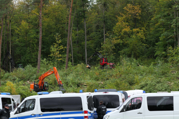 Polizeifahrzeuge in einem waldigen Gebiet geparkt, mit Officers in M√∞tzen und Jacken in der Nähe, ein Bagger im Hintergrund und Täler in der Umgebung unter einem offenen Himmel.