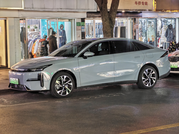 Ein Mitsubishi Lancer EV auf einer nächtlichen Stadtstraße geparkt, umgeben von Gebäuden, Schaufenstern, Schaufensterpuppen und beleuchteten Schildern.