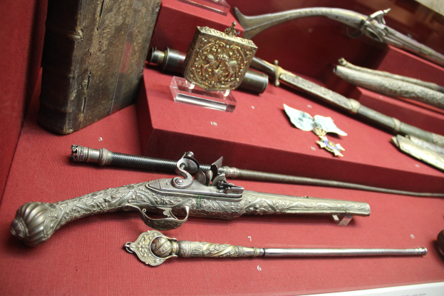 Vitrine mit verschiedenen Waffen, darunter ein Steinschlossgewehr, ordentlich auf einem roten Tisch angeordnet.