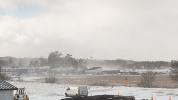 Ein weißer Lastwagen neben einem Gebäude in tiefem Schnee geparkt, mit Bäumen, Strommasten, Straßenlaternen und Baustoffen drumherum.