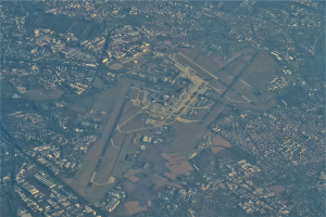 Eine Luftaufnahme eines Flughafens umgeben von Stadtgebäuden, Straßen und anderen Gegenständen mit Text am unteren Bildrand.