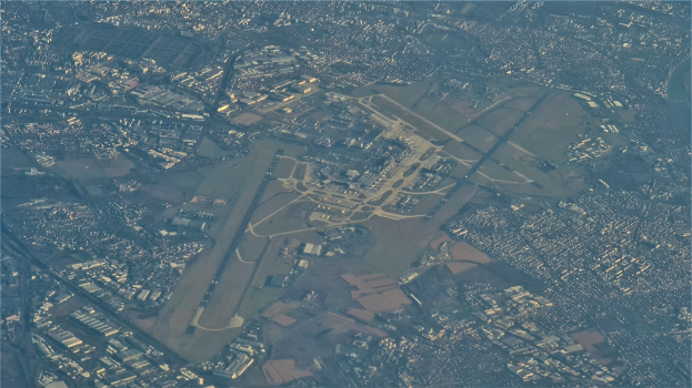 Eine Luftaufnahme eines Flughafens umgeben von Stadtgebäuden, Straßen und anderen Gegenständen mit Text am unteren Bildrand.