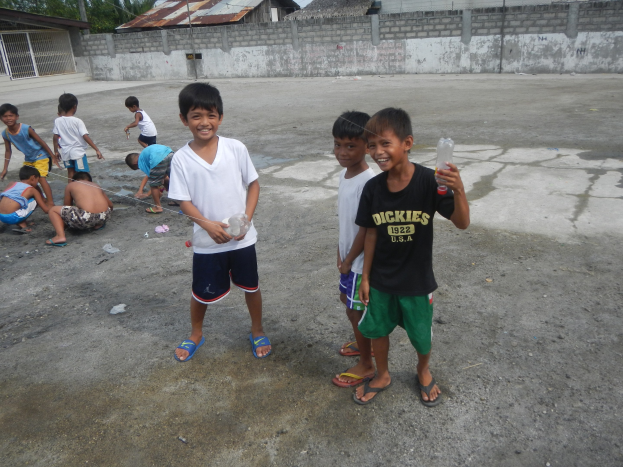Junge Jungs, die in einer Parklücke stehen und Flaschen halten, mit Häusern und Bäumen im Hintergrund bei klarem Himmel.