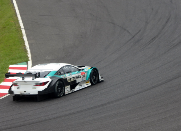 Ein Mercedes-AMG GT3 Rennwagen auf einer Rennstrecke mit Text auf seiner Karosserie und Gras links.