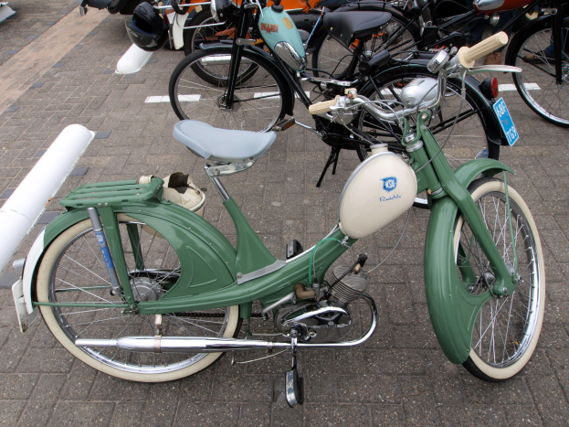 Ein grünes Moped mit einem weißen Rahmen und schwarzem Sitz neben anderen Motorrädern auf einem Gehweg geparkt, mit einigen Menschen in der Nähe.