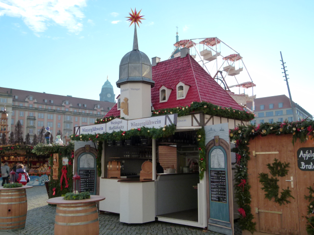 Kleines Gebäude mit rotem Dach und Riesenrad davor, umgeben von Festdekorationen und Menschen bei einem Outdoor-Event.
