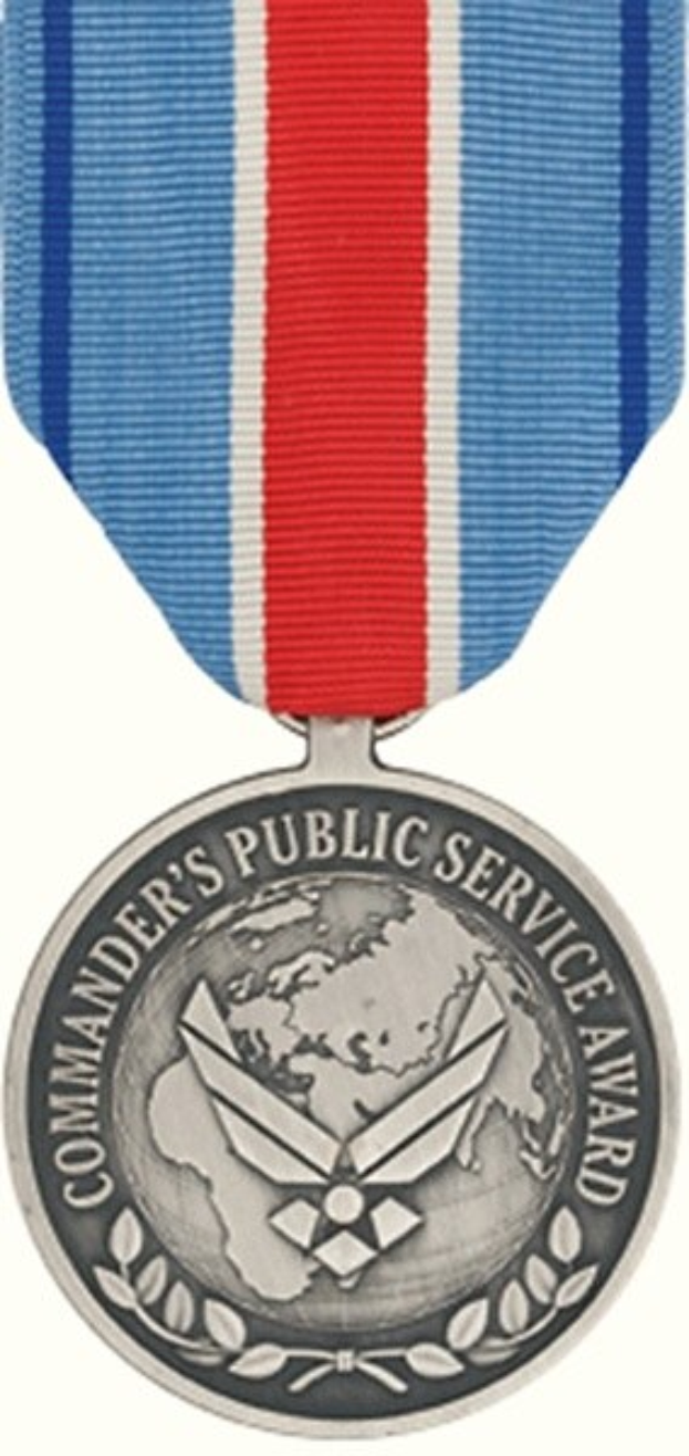 Eine silberne Medaille mit rot-weiß-blauem Band, darauf die Inschrift 'Commander's Public Service Award', vor weißem Hintergrund.