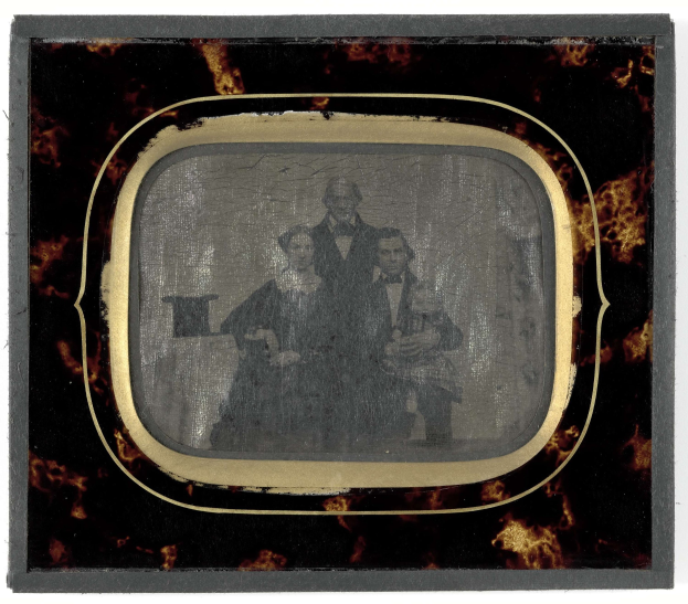 Schwarz-weiß-Foto eines Mannes im Anzug und einer Frau in unbekannter Kleidung, die vor einem Fernseher mit ernsten Gesichtern stehen.