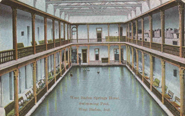 Alte Postkarte des großen Innenpools des West Baden Springs Hotels mit schwimmenden Menschen, umgeben von Säulen, Geländern, Stühlen und architektonischen Details, mit Text unten.