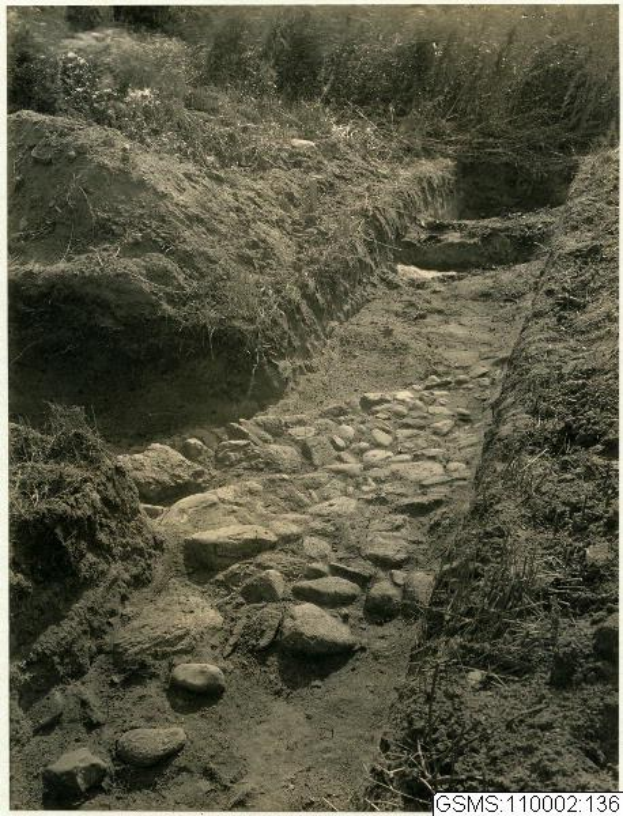 Schwarz-weißes Foto einer Schotterstraße, die durch ein Feld mit Steinen und Gras auf beiden Seiten führt, mit Text unten: "Der Weg nach oben".