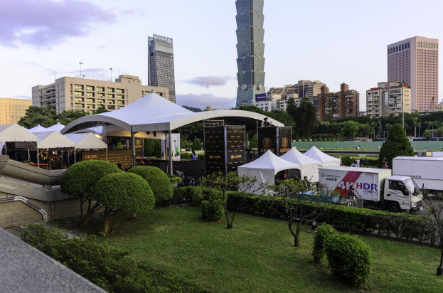Gruppe von Zelten in einem Park mit Grünflächen, Menschen, Fahrzeugen, Gebäuden und einem klaren Himmel, wahrscheinlich aufgenommen auf dem Hong Kong International Film Festival.