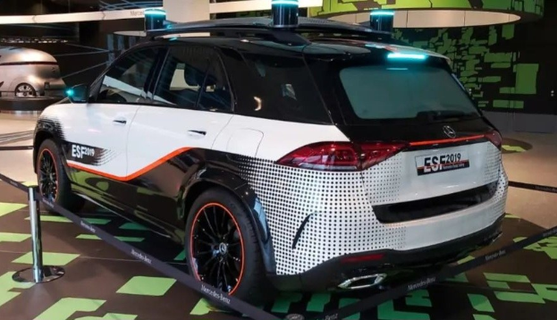 Mercedes-Benz E-Klasse Electric SUV auf der IAA in Frankfurt umgeben von Absperrgittern mit Seilen und Lichtern, mit einem weiteren Fahrzeug und einer textbedruckten Wand im Hintergrund.