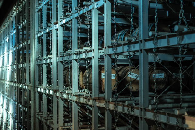 Großes Lager mit zahlreichen Fässern, die in Metallregalen gestapelt und durch Stangen und Ketten verbunden sind.