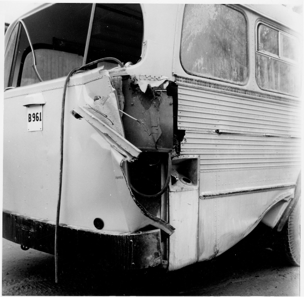 Schwarz-weiß-Foto eines Busses mit schwerer Frontschaden nach einem Autounfall, positioniert auf der Straße.