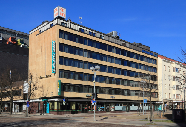 Großes Gebäude mit vielen Fenstern, identifiziert als das Fore Inn Hotel Berlin, umgeben von Straßeninfrastruktur und Bäumen unter einem bewölkten Himmel.