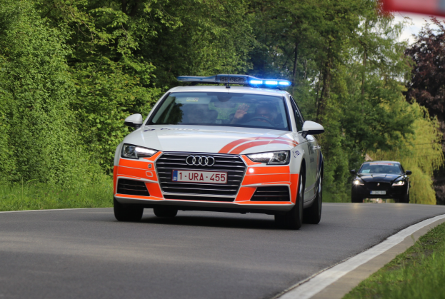 Polizeifahrzeug (Audi A4) mit zwei Insassen auf einer grasbewachsenen Straße neben einem Wald unter einem klaren blauen Himmel.