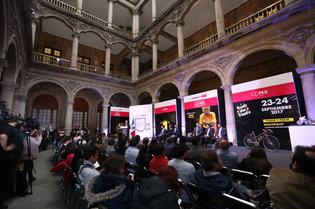Eine Gruppe von Menschen an einem Tisch mit einem Podium und Mikrofon vor einer Menge, Kameras und Bannern, was auf eine Pressekonferenz für das CDMX 2017-Event hindeutet.