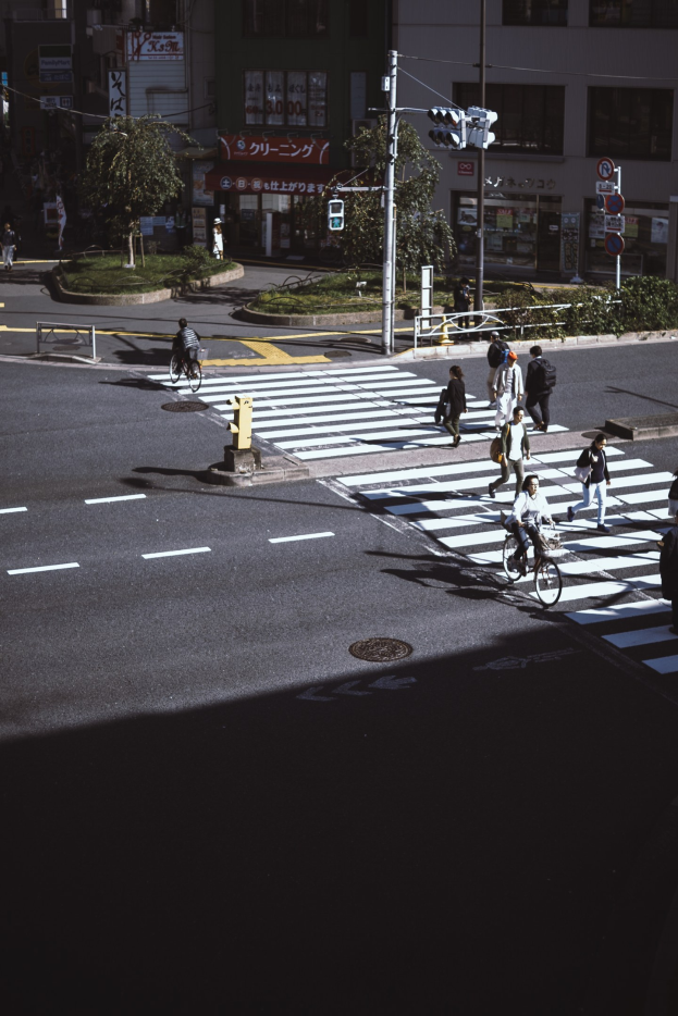 Gruppe von Menschen, die die Straße an einer Ampel überqueren, mit einem Radfahrer im Vordergrund, Gebäude und Bäume im Hintergrund.