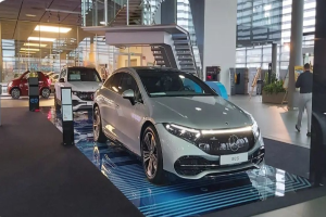 Ein Mercedes-Benz S-Klasse Coupé wird auf der IAA in Frankfurt umgeben von einer Glaswand, Treppen und Lichtern präsentiert, während mehrere Personen das Auto bewundern.
