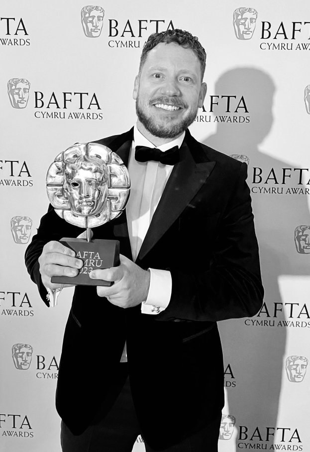 Ein Mann in einem Smoking, der eine BAFTA-Trophäe hält und lächelt, mit einem Hintergrundschild, auf dem "BAFTA Awards 2018" steht
