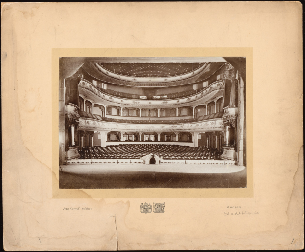 Schwarzes und weißes Foto des Auditoriums der Royal Albert Hall in London, das die Bühne, Sitzreihen, Säulen, Geländer und Text mit einem Logo unten zeigt.