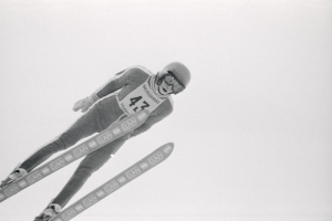Skispringer in voller Ausr├╝stung springt in der Luft auf Skiern gegen einen klaren blauen Himmel