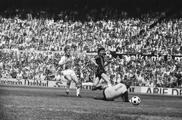 Schwarzes Foto von Männern, die auf einem Feld Fußball spielen, mit Zuschauern im Hintergrund und einem Banner mit der Aufschrift "Bundesliga 1978-79 Ajax 1-1 Hannover 96".