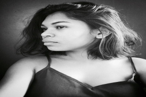 Eine selbstbewusste Frau in einem schwarzen Kleid posiert in einem Schwarz-Weiß-Foto vor einer Wand mit einem eleganten Bob und natürlichem Make-up.