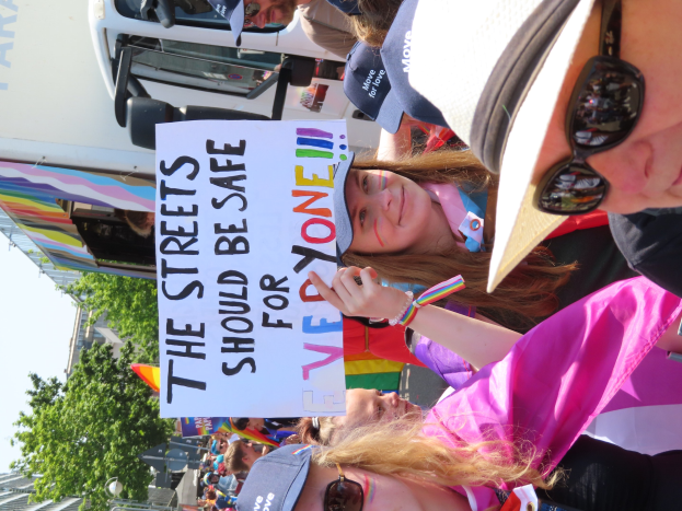Eine Gruppe von Menschen mit einer Tafel "Die Straßen sollten sicher sein" vor einem Lkw, einige tragen Mönen und Schutzbrillen, andere halten Schilder, vor einem Hintergrund aus Bäumen, Gebäuden und einem klaren blauen Himmel.