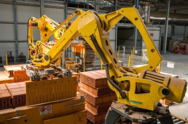 Großes industrielles Lager mit gestapelten Kisten, Überkopfkranen, Zaun, Strommasten und einer fernen Wand in einer Fertigungsanlage.