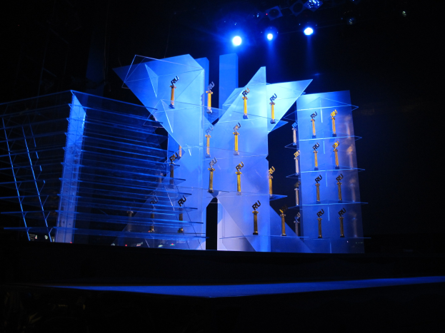 Eine Bühne für eine Preisverleihung mit dunklem Hintergrund, beleuchtet von ein paar Lichtern, mit Gegenständen, die wahrscheinlich mit dem Ereignis zu tun haben.