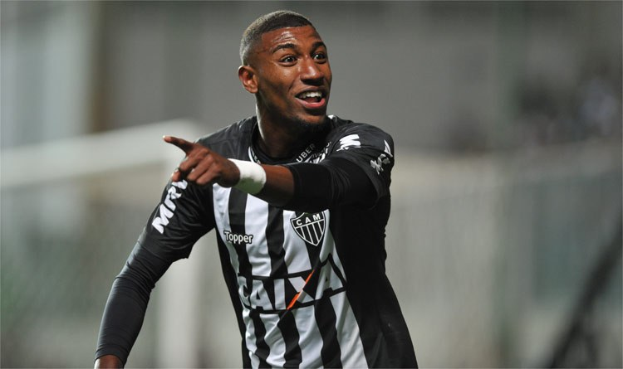 Ein Fußballspieler in einem schwarzen und weißen gestreiftem T-Shirt feiert ein Tor, strahlend mit einem unscharfen Hintergrund.