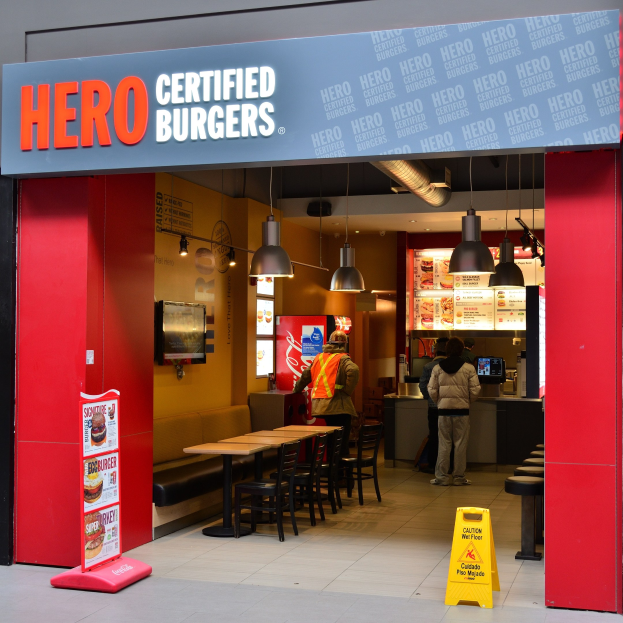 Außenansicht eines Hero Certified Burgers Restaurants in London mit Gästen, Sitzplätzen, einer Speisekarte, einem wandmontierten Fernseher und Deckenbeleuchtung.