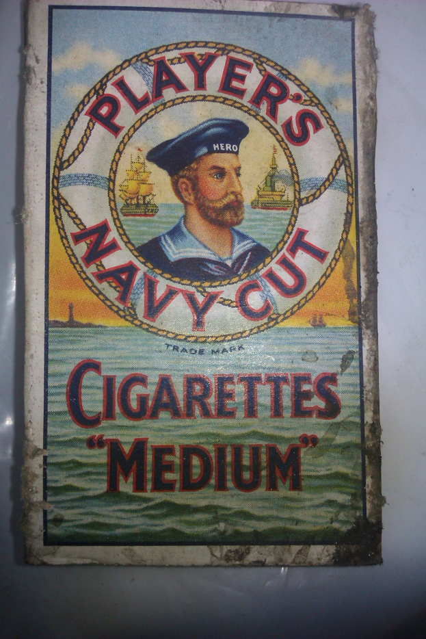 Plakat, das "Player's Navy Cut Cigarettes Medium" bewirbt, zeigt eine Person in einer marineblauen Uniform mit weißem Hemd und roter Krawatte, die Arme verschränkt und einen strengen Gesichtsausdruck hat, Text in fetter schwarzer Schrift innerhalb eines weißen Rahmens.