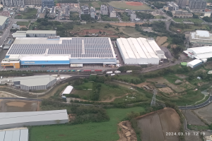 Eine Luftaufnahme eines großen Industriegebiets mit Gebäuden, Bäumen, Gras, Straßen, Fahrzeugen, Masten und einem Wasserzeichen, das es sich um die erste Solarstromanlage in Singapur handelt, in der unteren rechten Ecke.