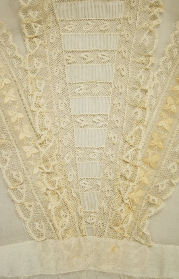 Nahaufnahme eines weißen Kleides mit zarter, kunstvoller Spitzenverzierung mit verschiedenen Mustern auf einem leichten, luftigen Stoff.